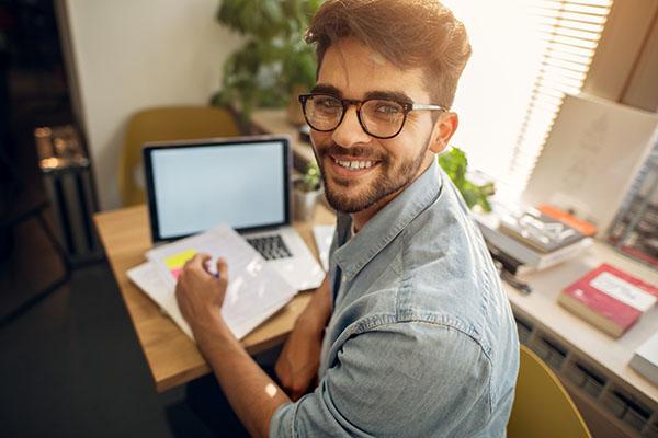 Student taking notes from a laptop turns to smile at camera